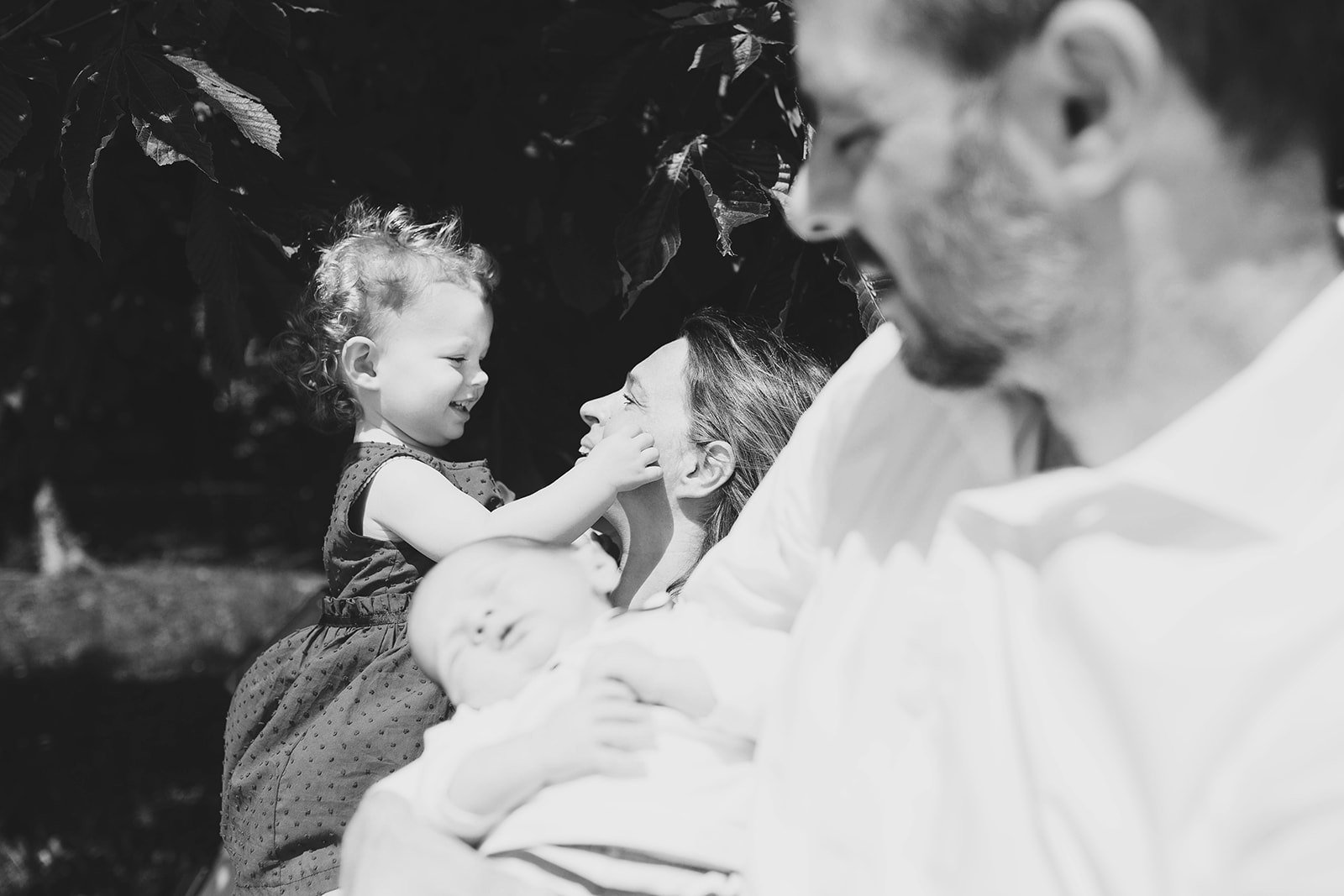 foto di famiglia in bianco e nero, mamma e figlia sul fondo a fuoco che si guardano dolcemente, in primo piano papà e figlio sfuocati. Fotografa Deborah Brugnera